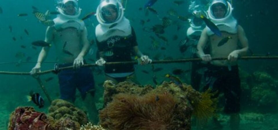 A group of tourists wearing helmets and walking underwater at Manukan Island, one of the best islands in Sabah for snorkeling and diving.