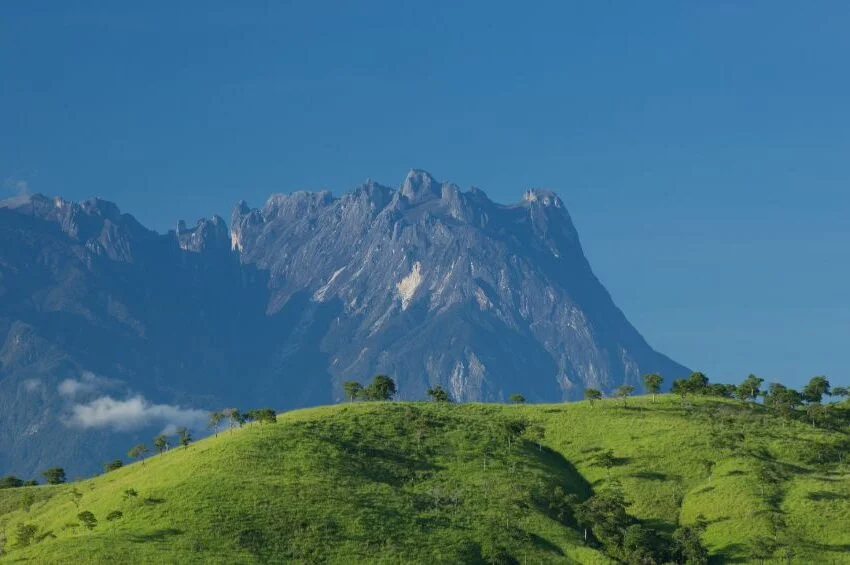 A scenic view of Mount Kinabalu peak with clouds and greenery