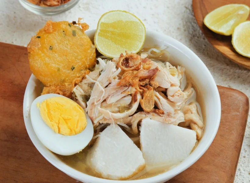 Bowl of Soto Banjar in Sandakan, showcasing clear spiced broth, chicken, noodles, and herbs — a dish influenced by Indonesian heritage.