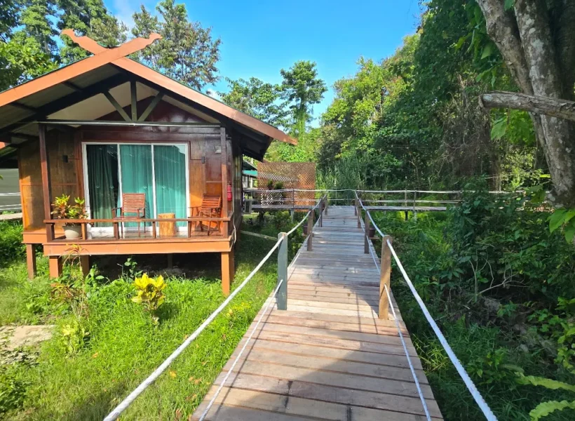 Wooden walkway leading to chalets at Nature Lodge Kinabatangan, a nature-inspired accommodation surrounded by tropical greenery.